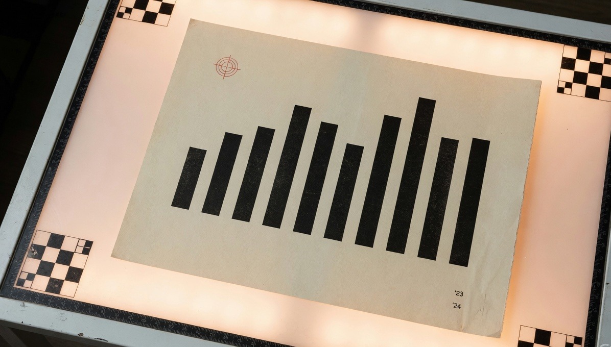 A cream year-in-review print on a photographer's light table, twelve black bars and a vermilion registration mark.