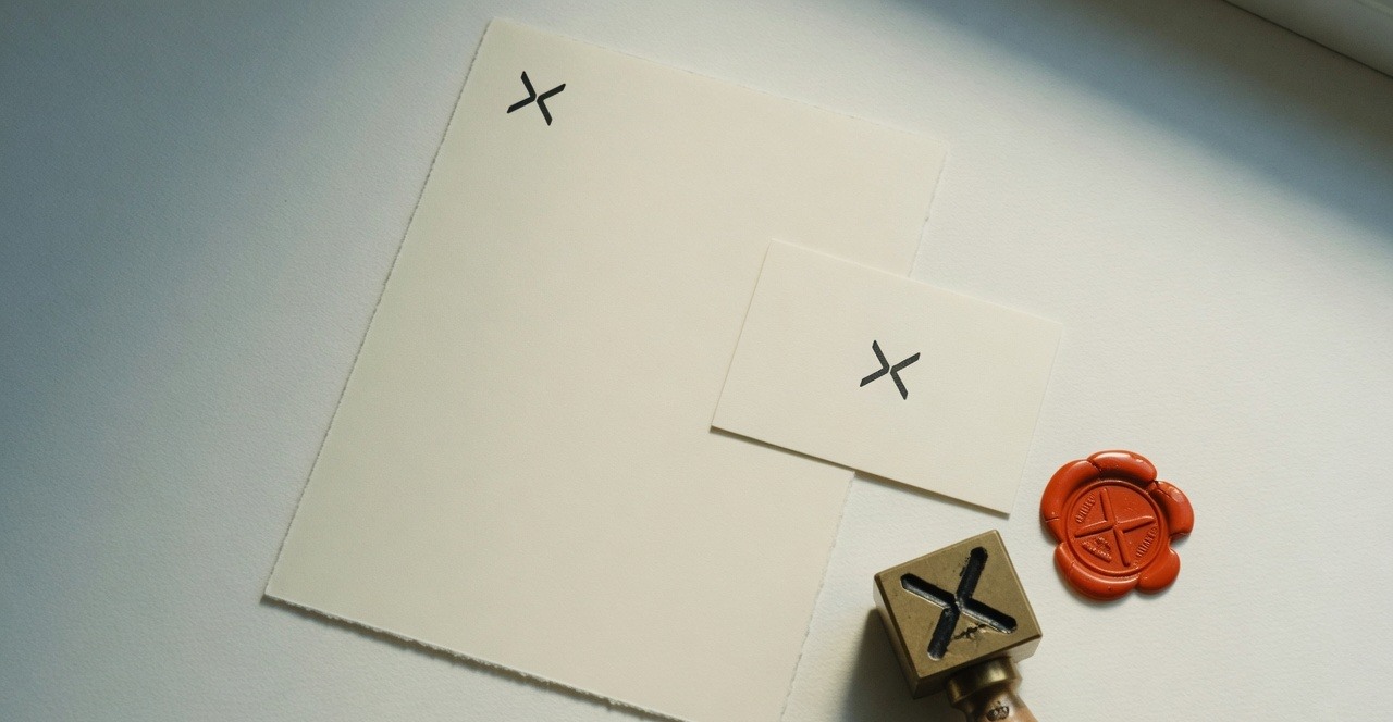 Cream letterhead and card with a split-X mark, a matching brass stamp and vermilion wax seal.