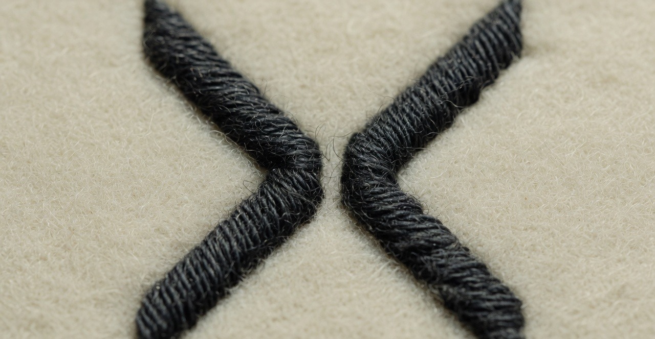 Close-up of the split-X mark stitched in dark thread on cream wool.